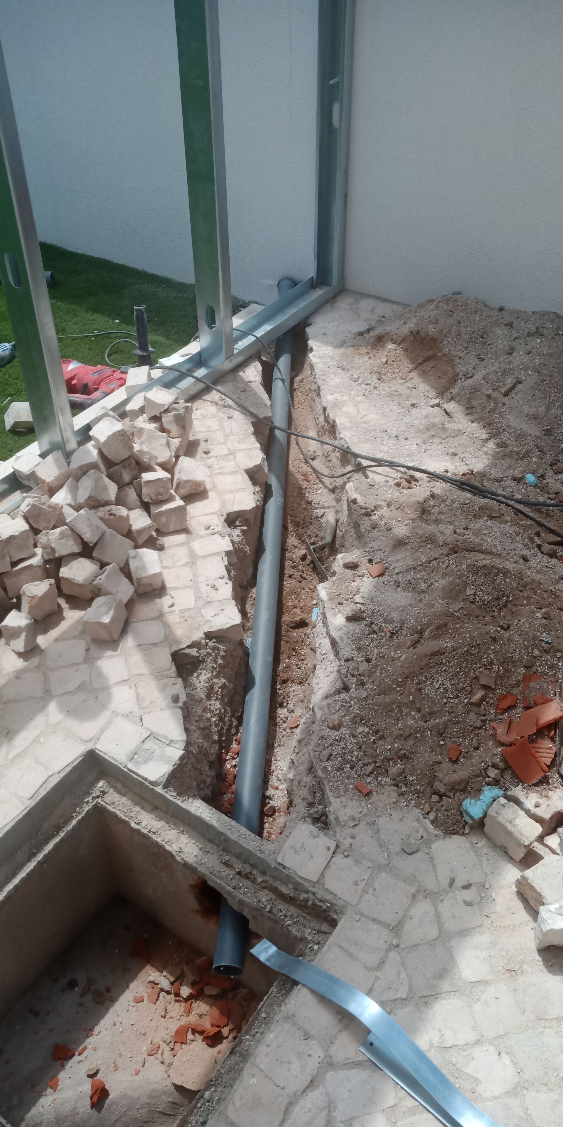 Uma vala com canos percorre uma parede. Tijolos e cascalho cercam os canos. Canteiro de obras.