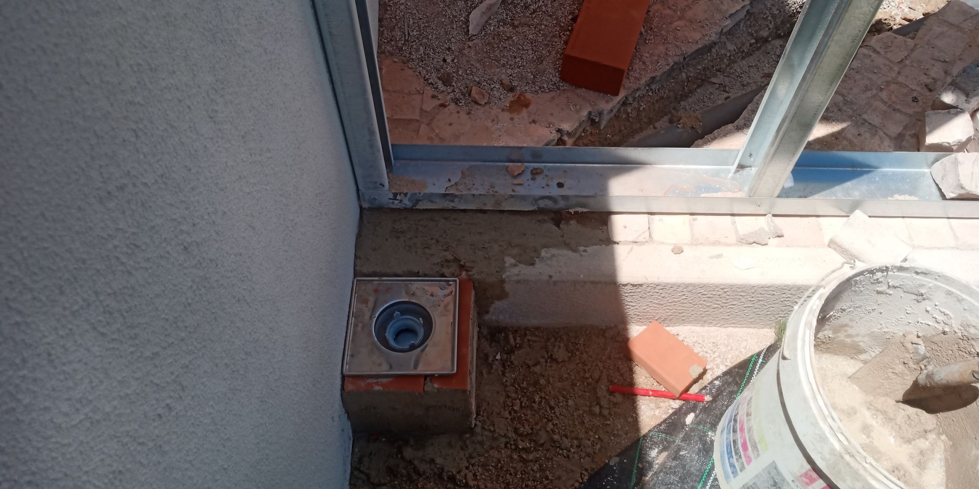 Canteiro de obras com parede, estrutura metálica, dreno, tijolo e balde.