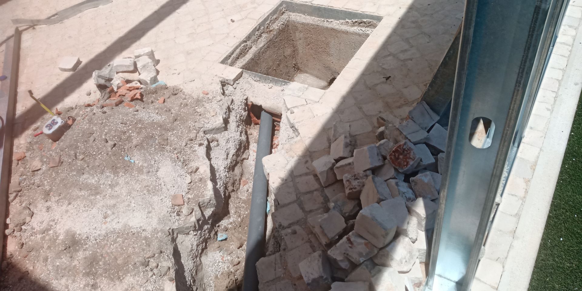 Canteiro de obras com terreno escavado, tijolos espalhados e uma viga metálica.