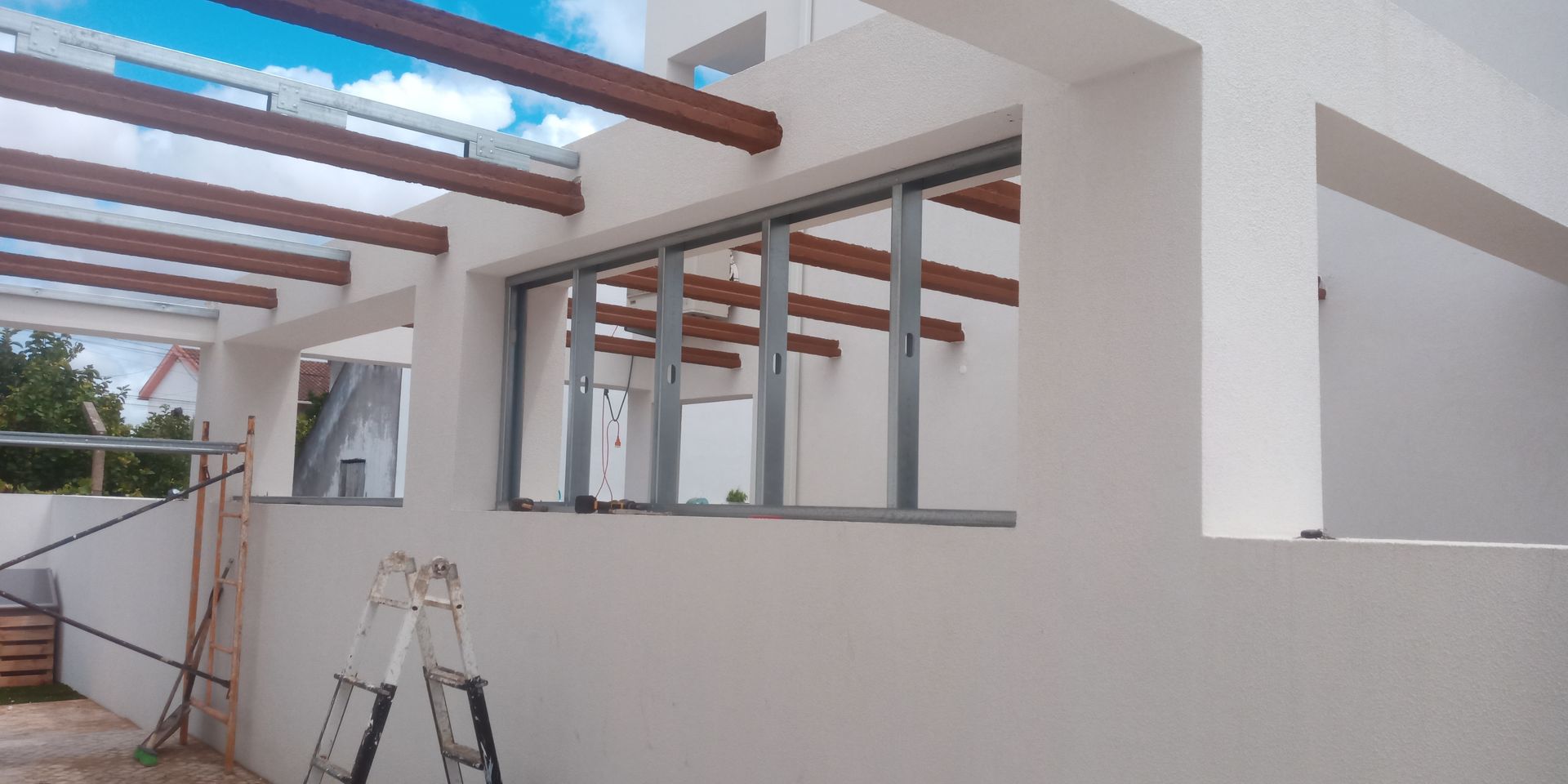 Exterior de um edifício branco com vigas expostas, grandes janelas e andaimes.