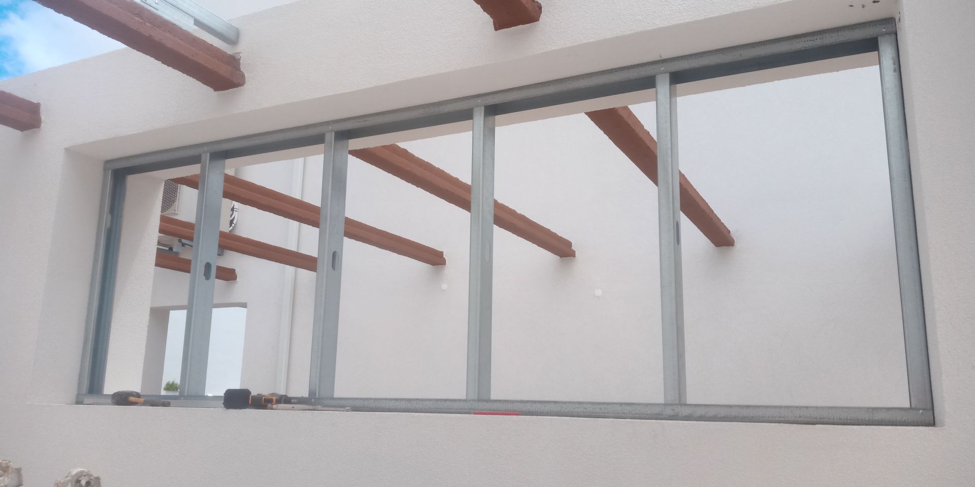 Exterior de um edifício com uma grande porta de vidro deslizante, paredes brancas e vigas de madeira.