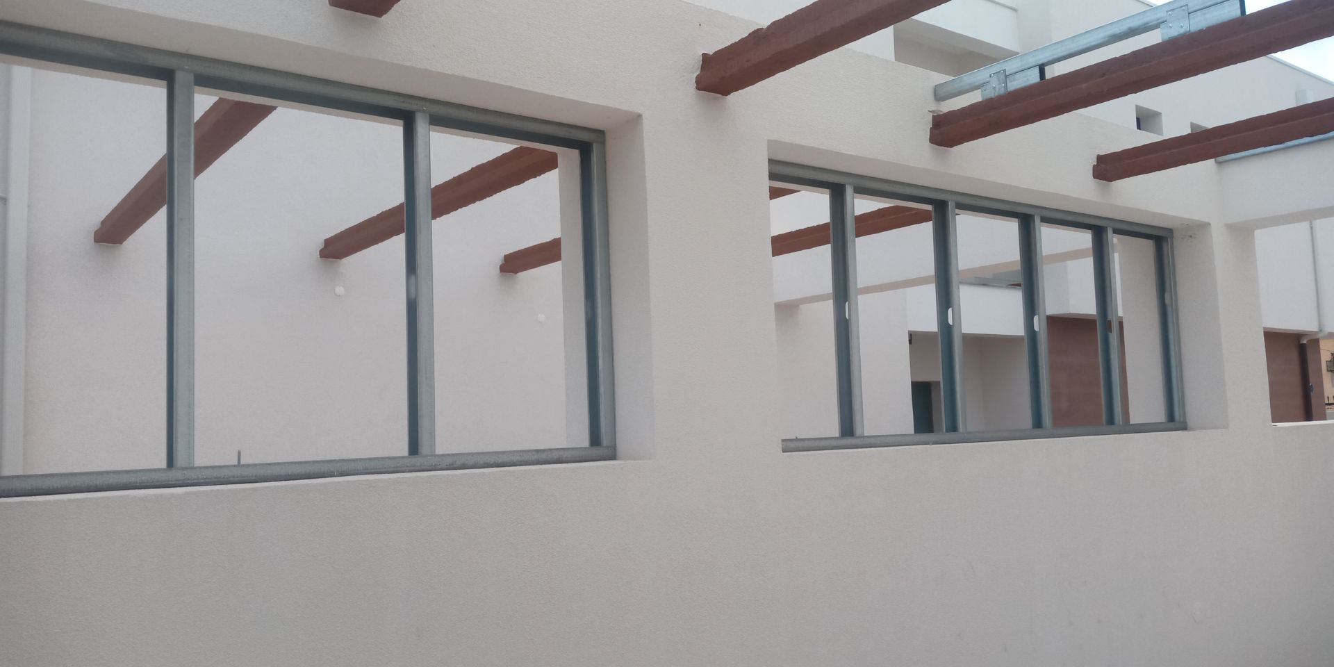 Vista exterior de um edifício com várias janelas de vidro e vigas de madeira castanhas. As paredes são brancas.