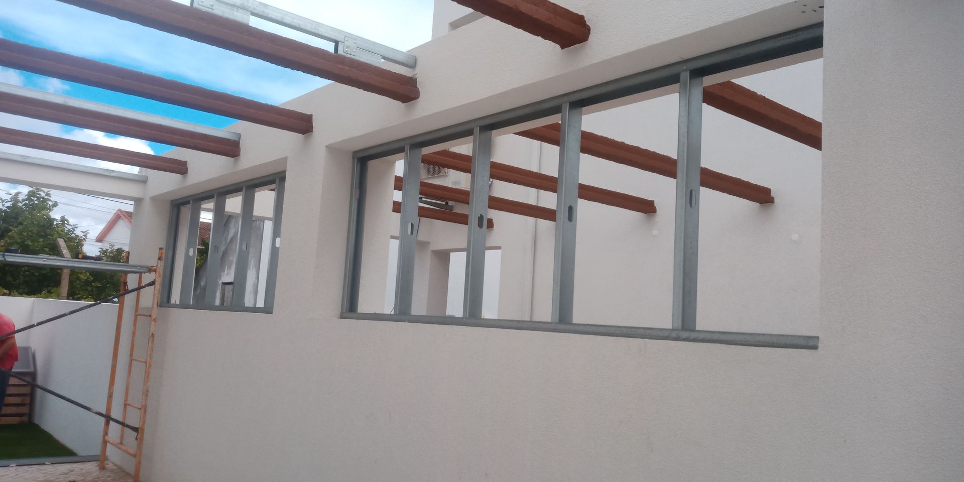 Vista exterior de um edifício com múltiplas janelas e vigas de madeira que sustentam um telhado translúcido.