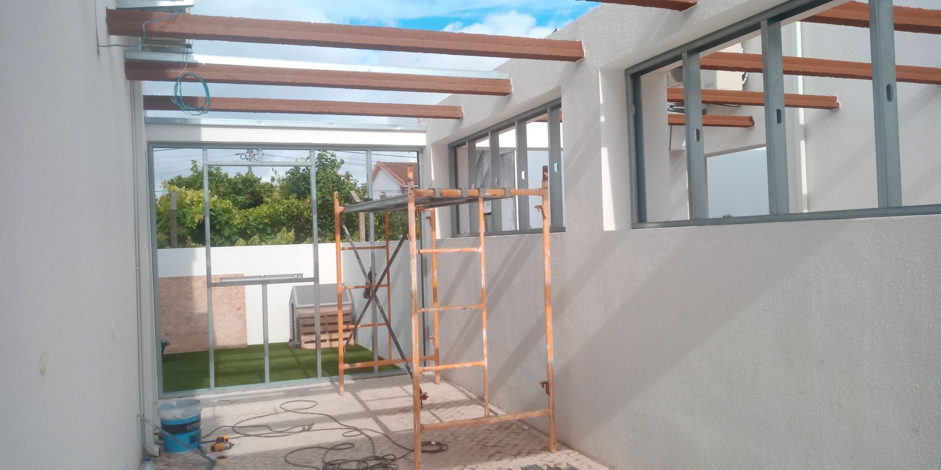 Construção de um espaço exterior com vigas de madeira, estrutura metálica e cobertura parcialmente transparente.