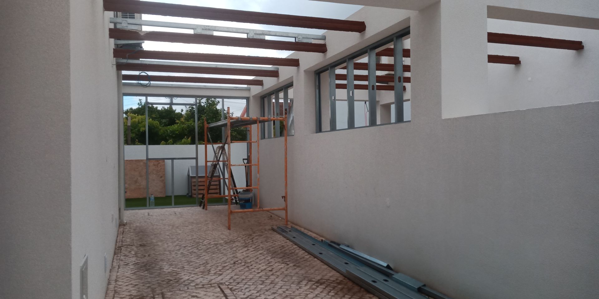 Espaço externo coberto com piso de pedra, janelas de vidro e teto com vigas de madeira.