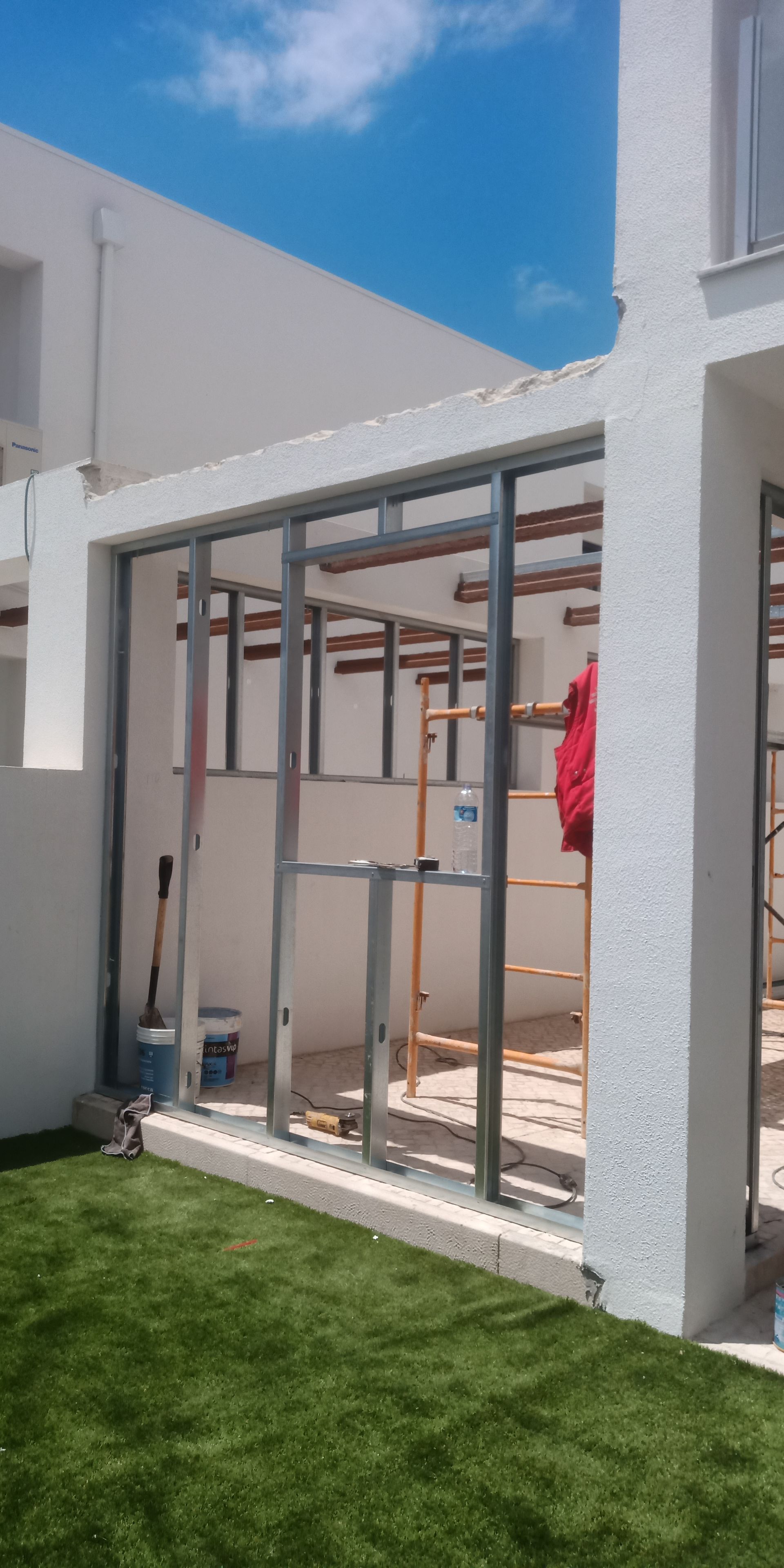 Um edifício em construção com estrutura de aço, rodeado de grama e céu azul.