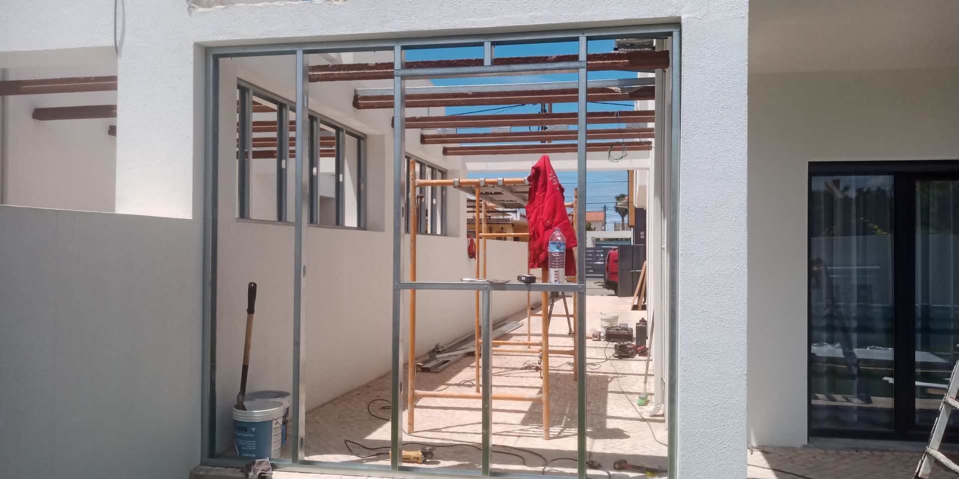 Canteiro de obras com estrutura metálica para porta de correr. Jaqueta vermelha pendurada em uma escada.
