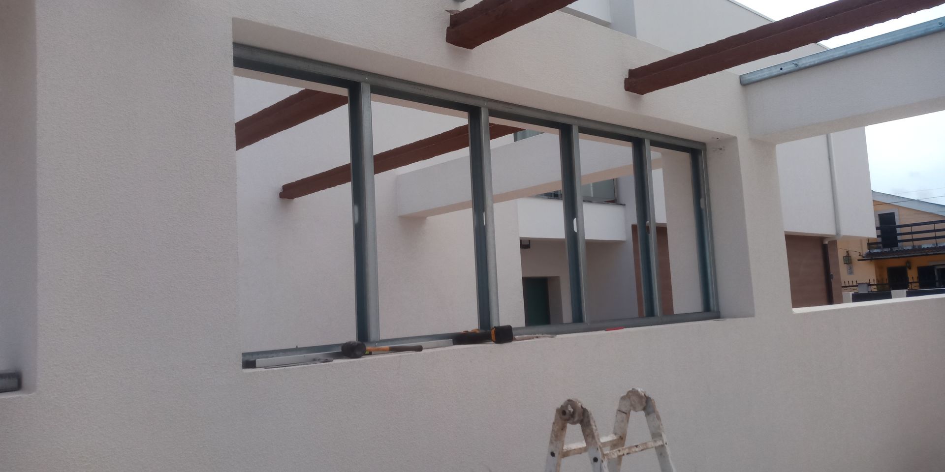 Vista exterior de um edifício em construção, apresentando uma moldura de janela, vigas de madeira e uma escada.