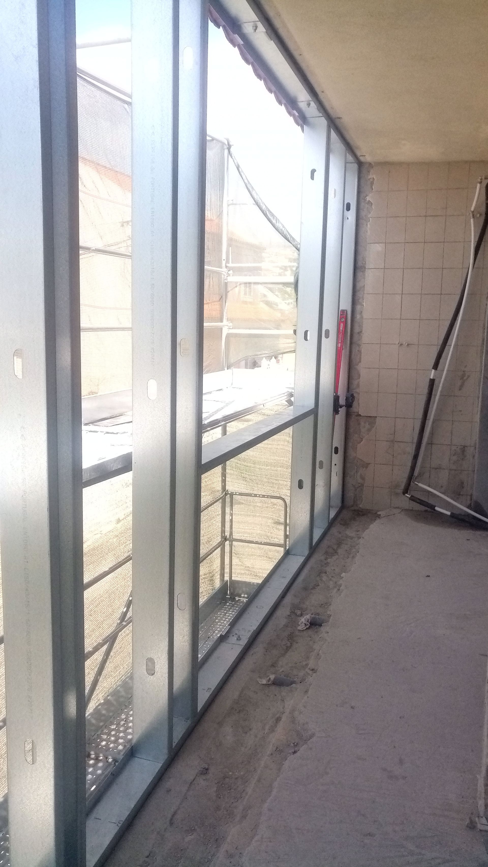 Estrutura da parede interna com perfis metálicos e janela aparente, em construção.