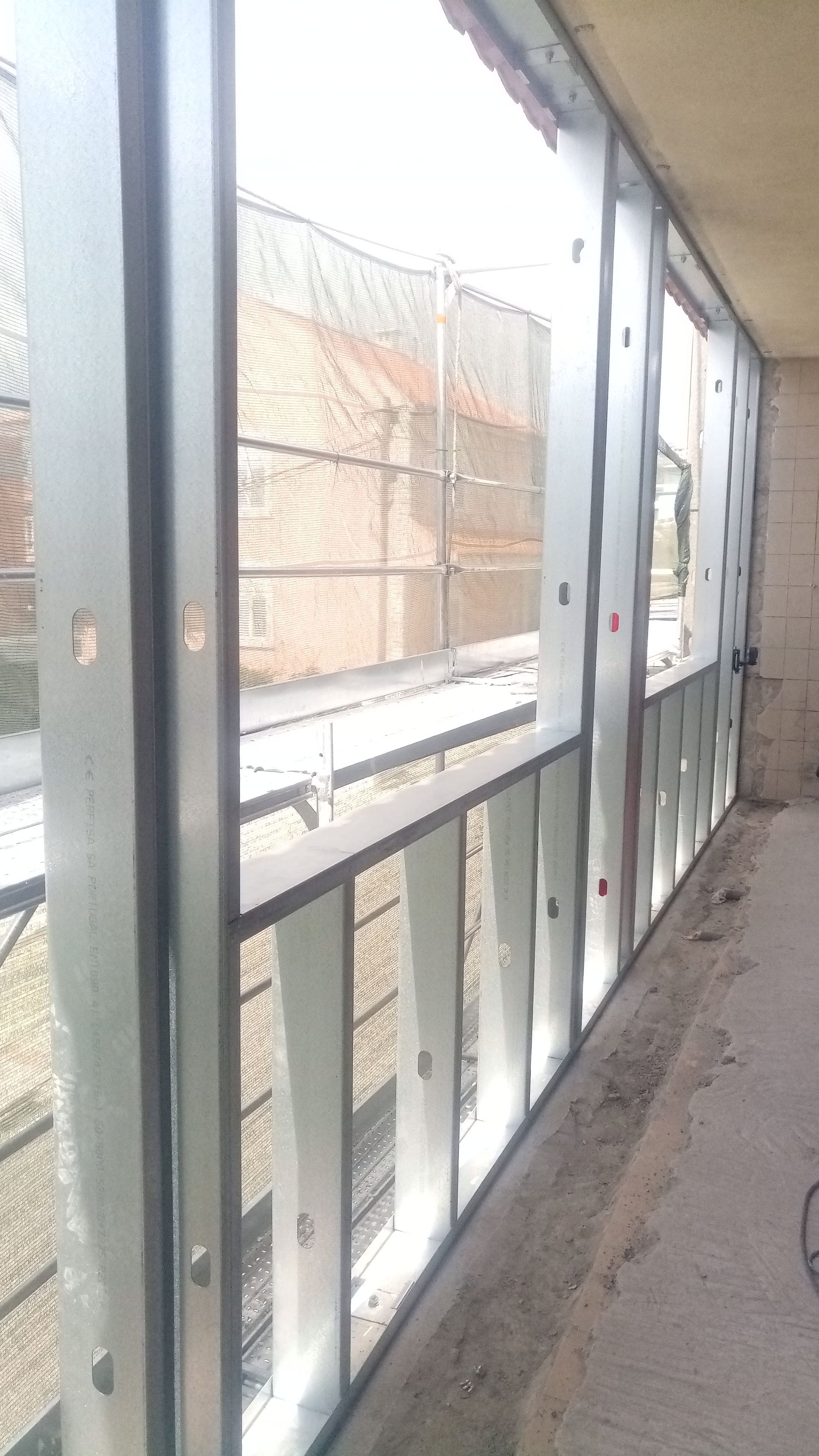 Estrutura metálica para abertura de janela em um prédio em construção, com cerca de arame visível do lado de fora.