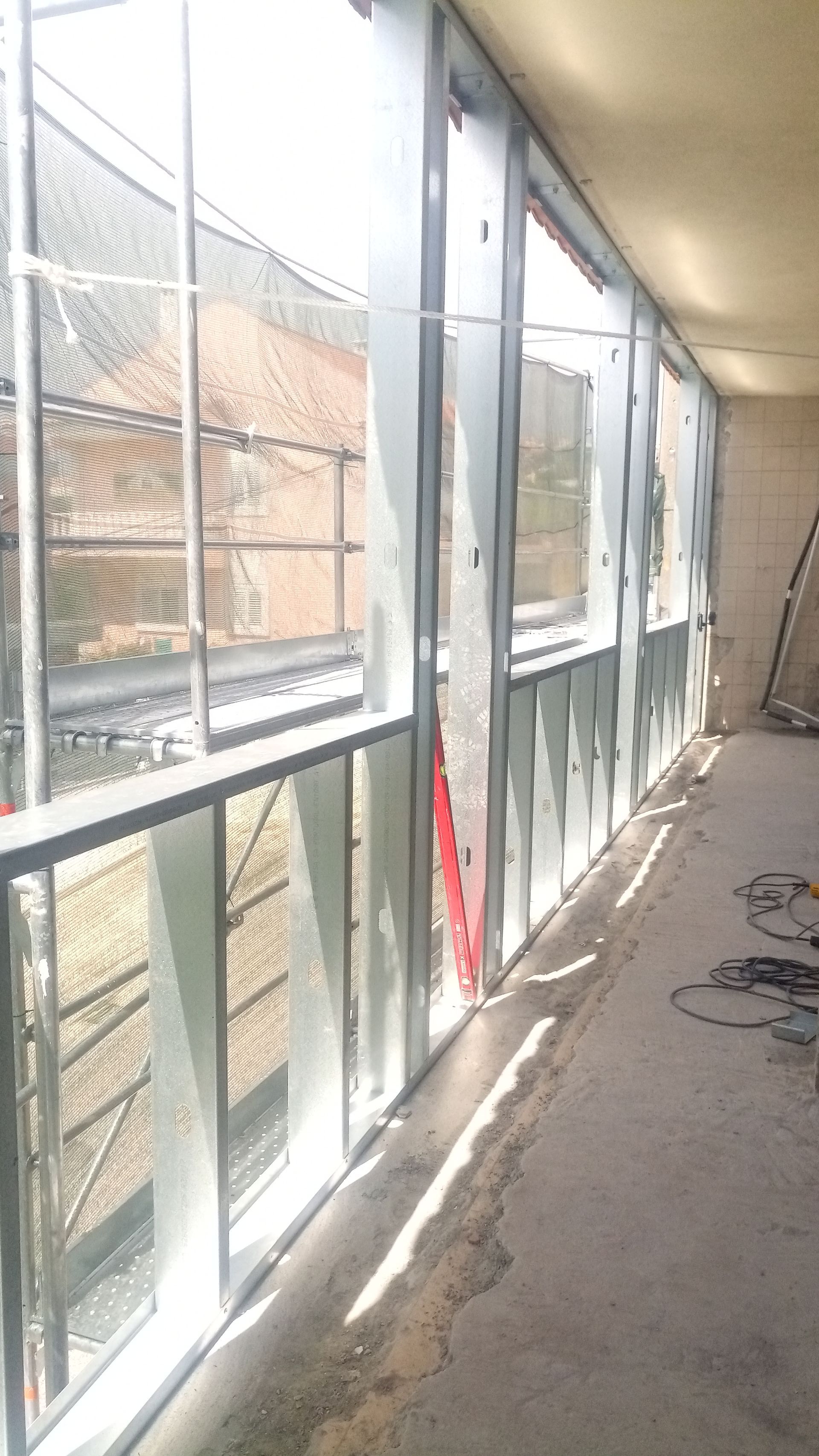 Corredor com janelas de vidro parcialmente instaladas, estrutura metálica e piso de concreto.