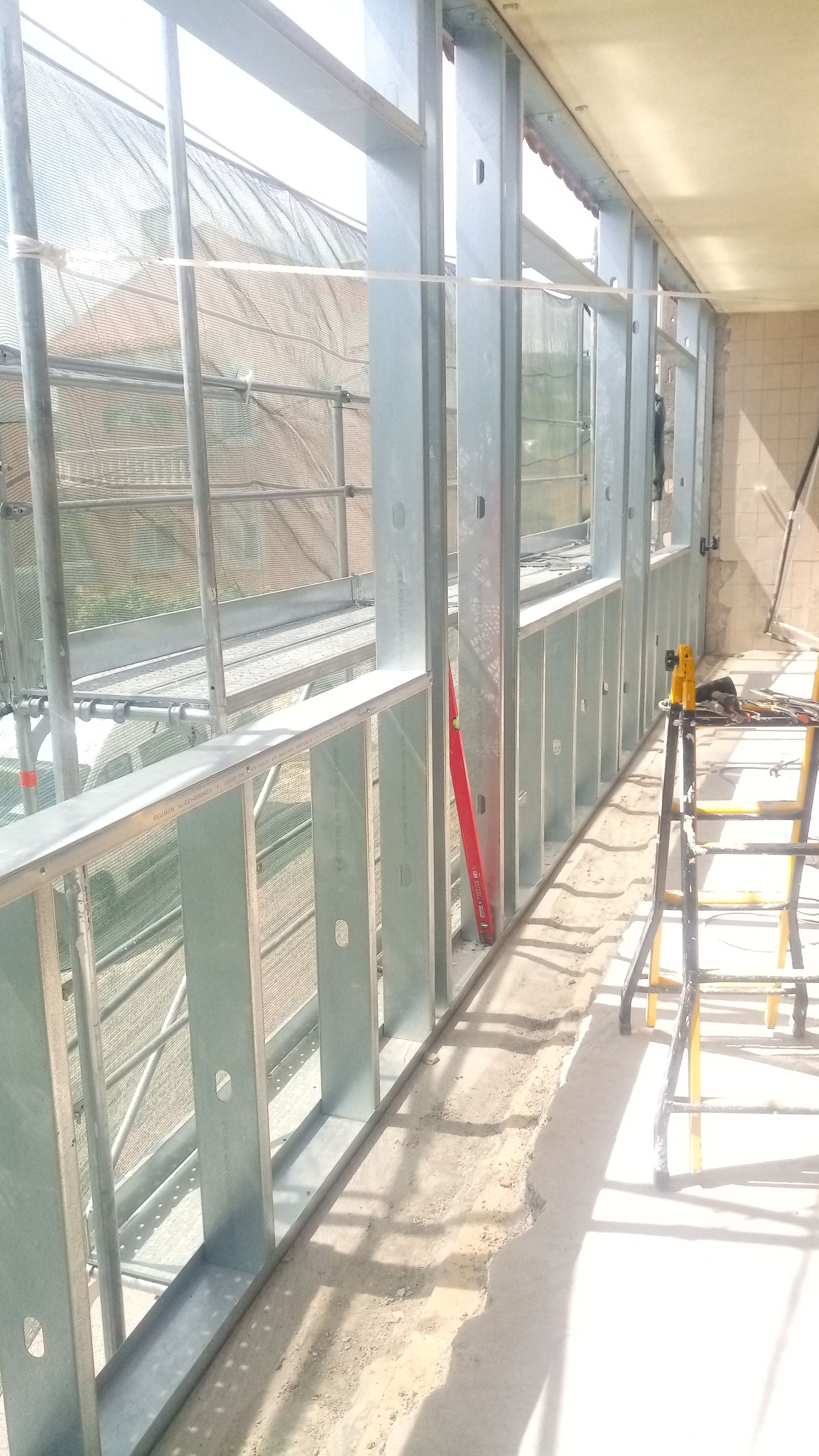 Estrutura metálica da parede de um edifício, com janelas instaladas. Um nível está encostado em uma viga.