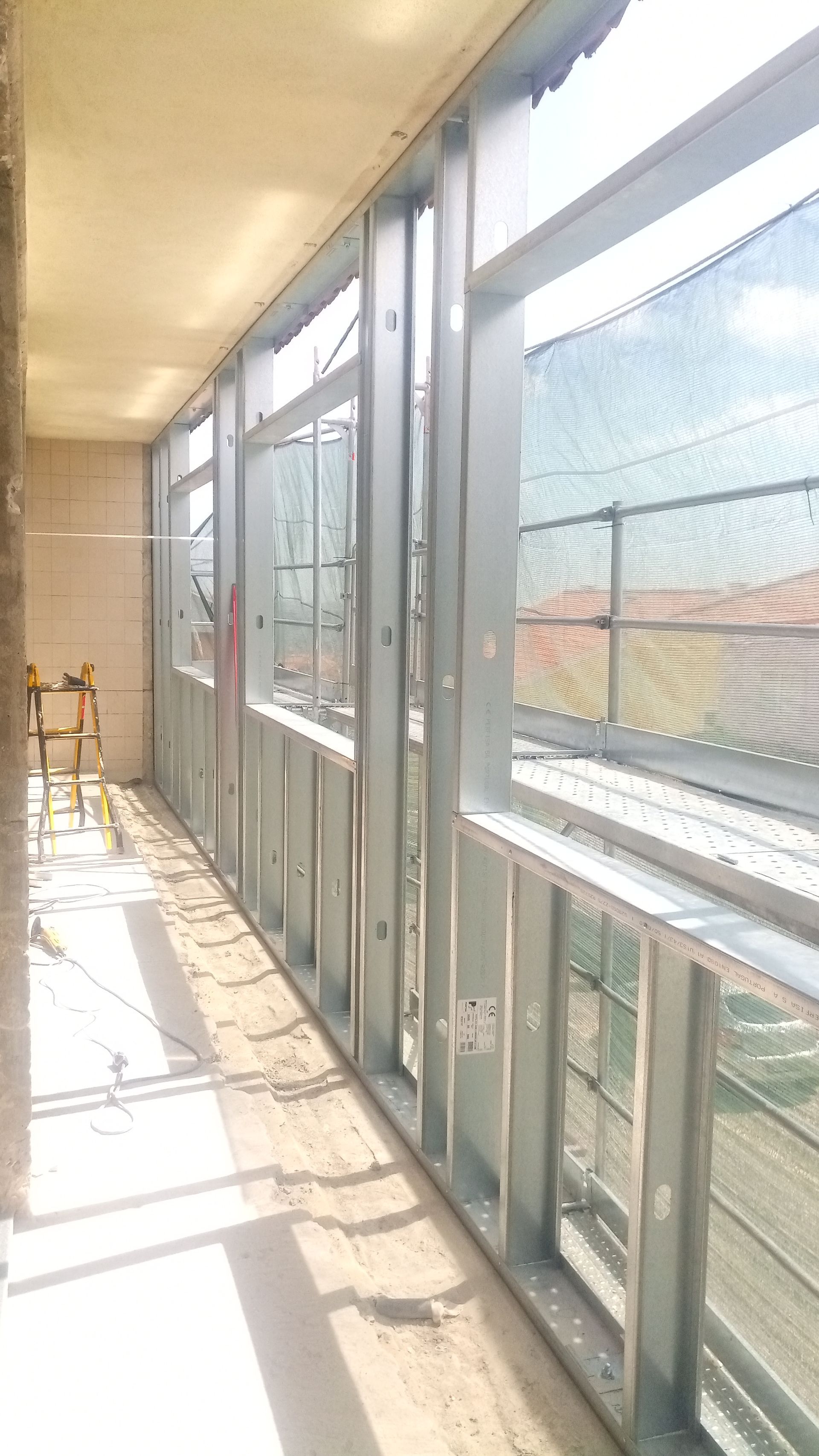 Estrutura metálica de uma varanda envidraçada em construção, com vista para a paisagem urbana.