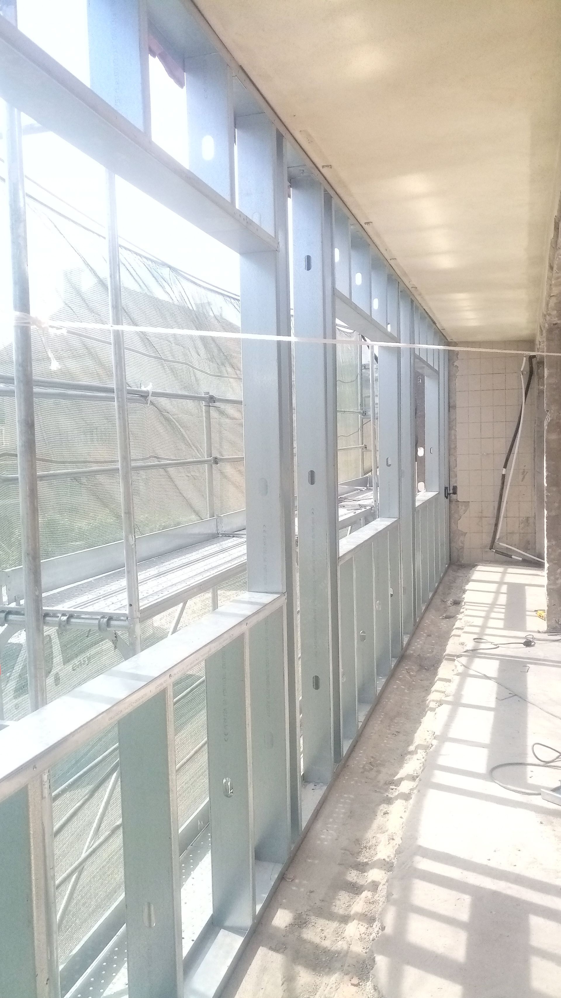 Estrutura metálica do interior de um edifício com janelas e paredes inacabadas.