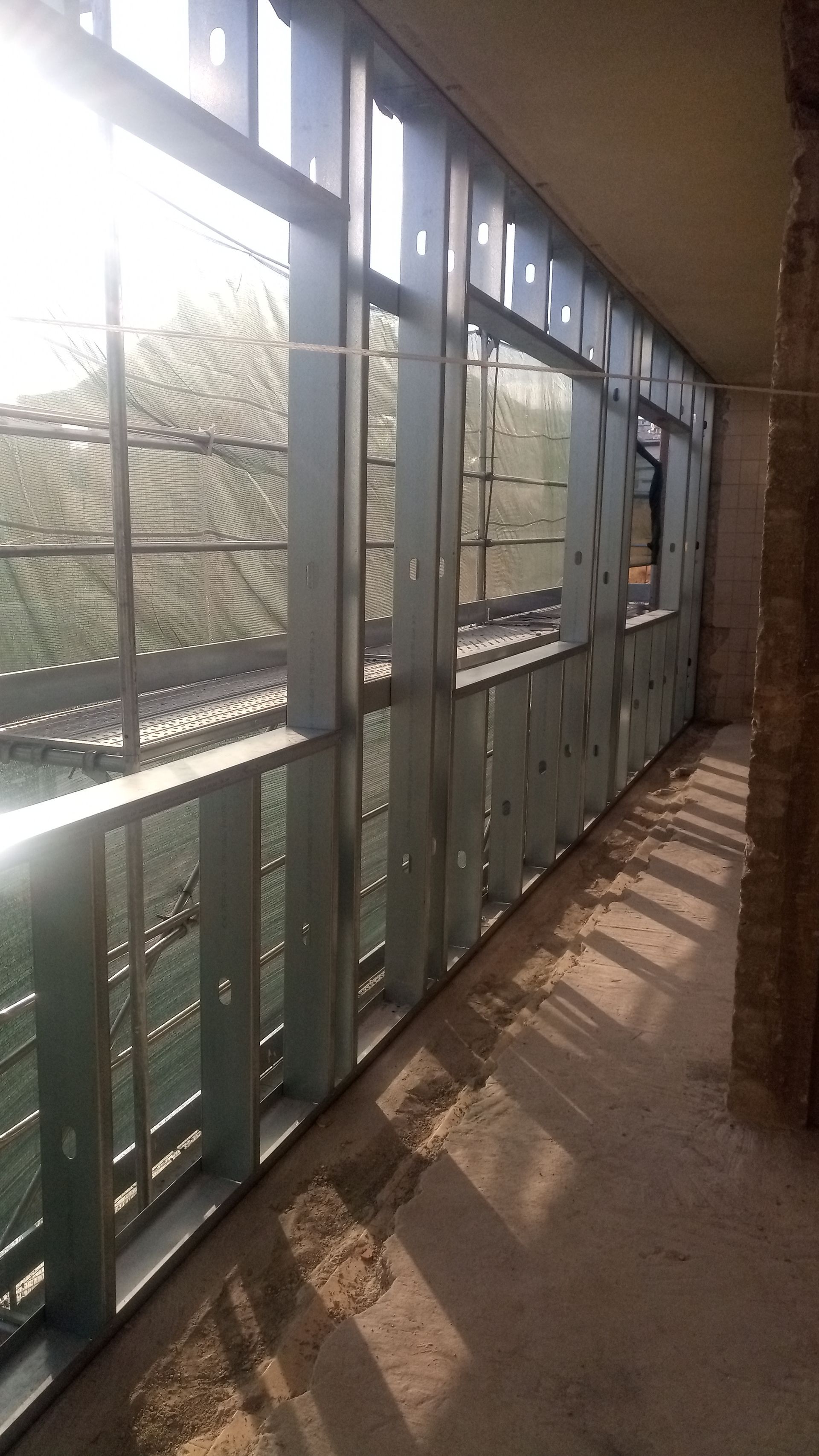 Interior de um canteiro de obras com estrutura metálica, isolamento e janelas.