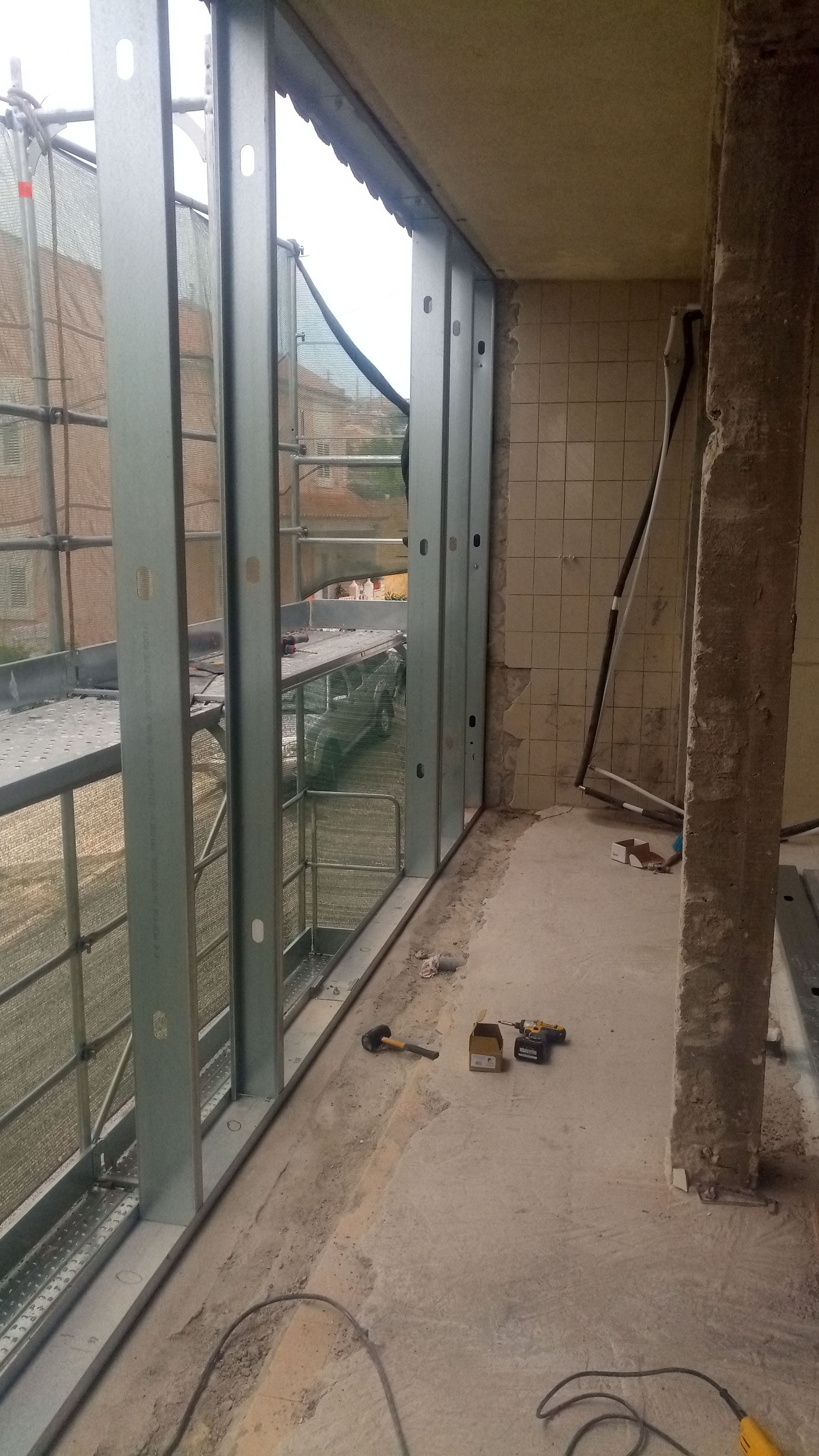 Vista interna do canteiro de obras. Caixilhos de metal instalados, piso e paredes de concreto inacabados.