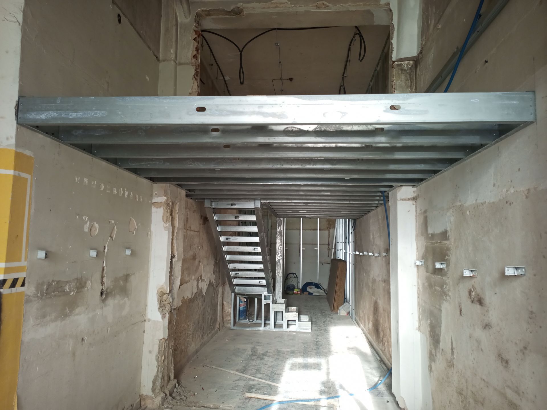 Foto do interior de um cômodo em construção com estrutura metálica para um mezanino. Uma escada é visível.