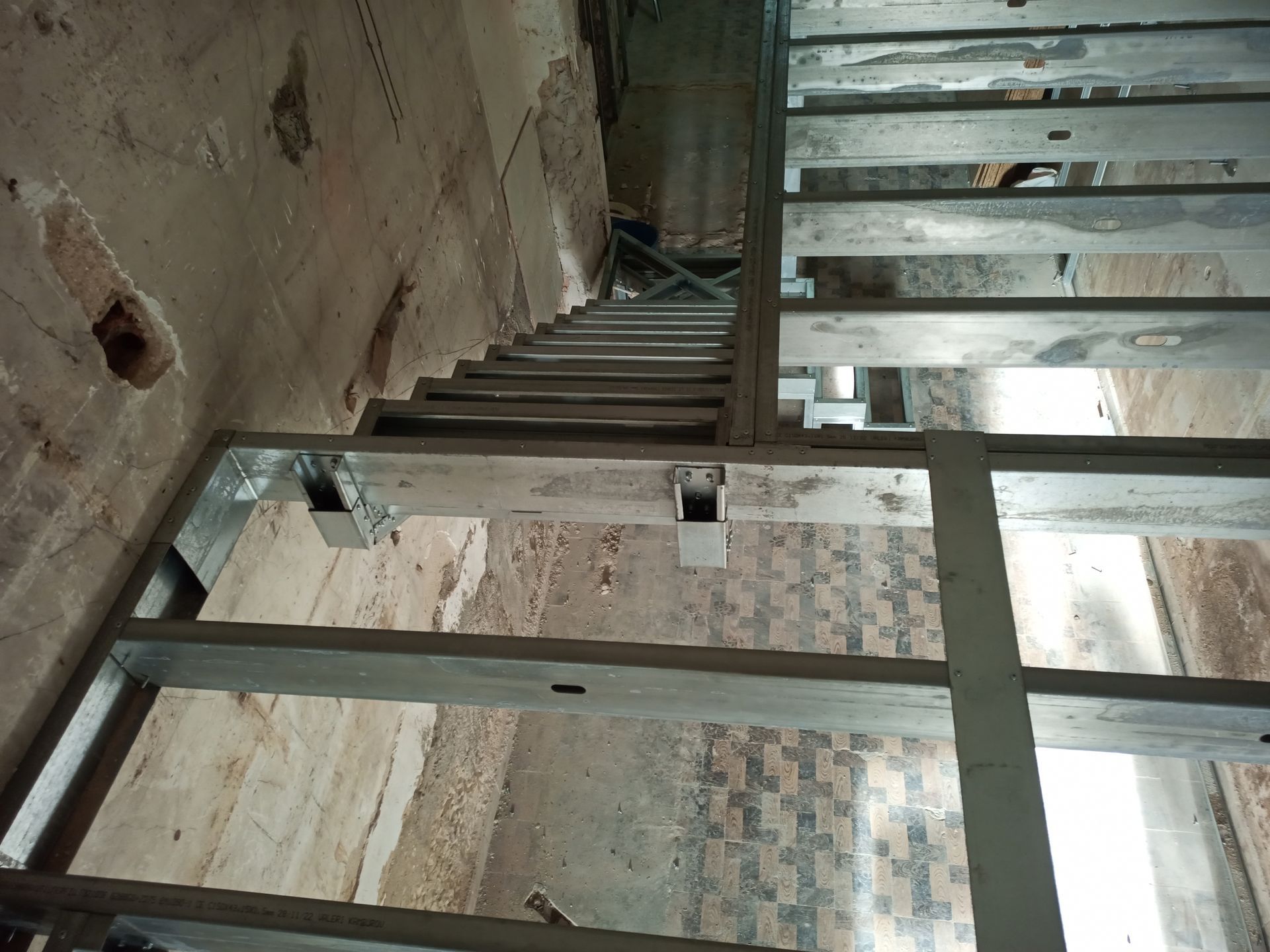 Escada metálica em um prédio com paredes de tijolo e concreto envelhecidas. A escada desce, vista de cima.