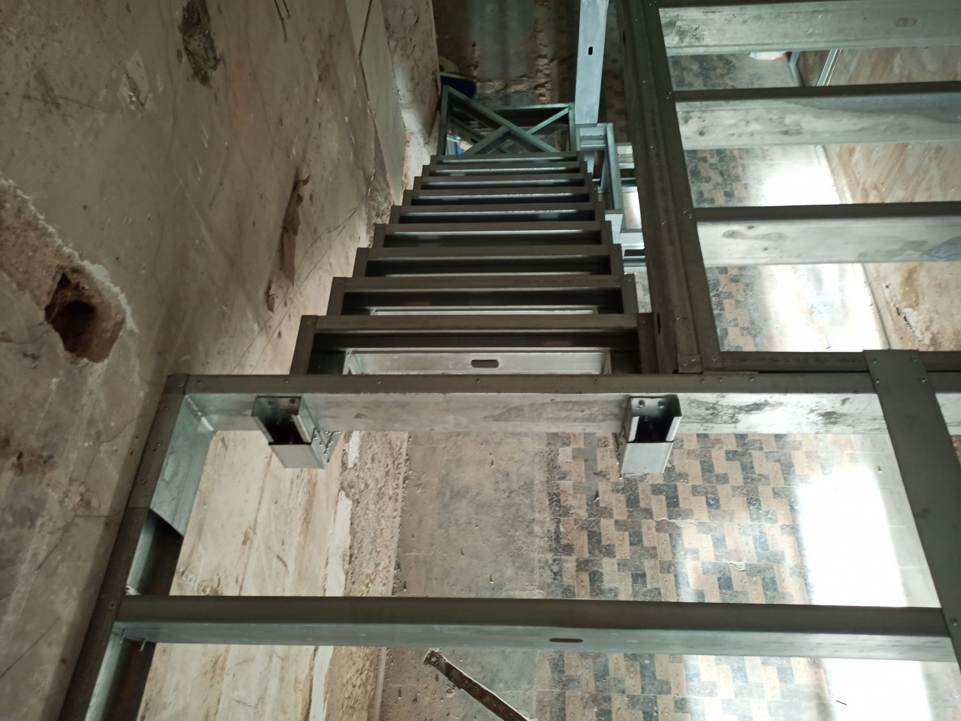 Escada metálica em construção, encostada em uma parede desgastada, vista de baixo.