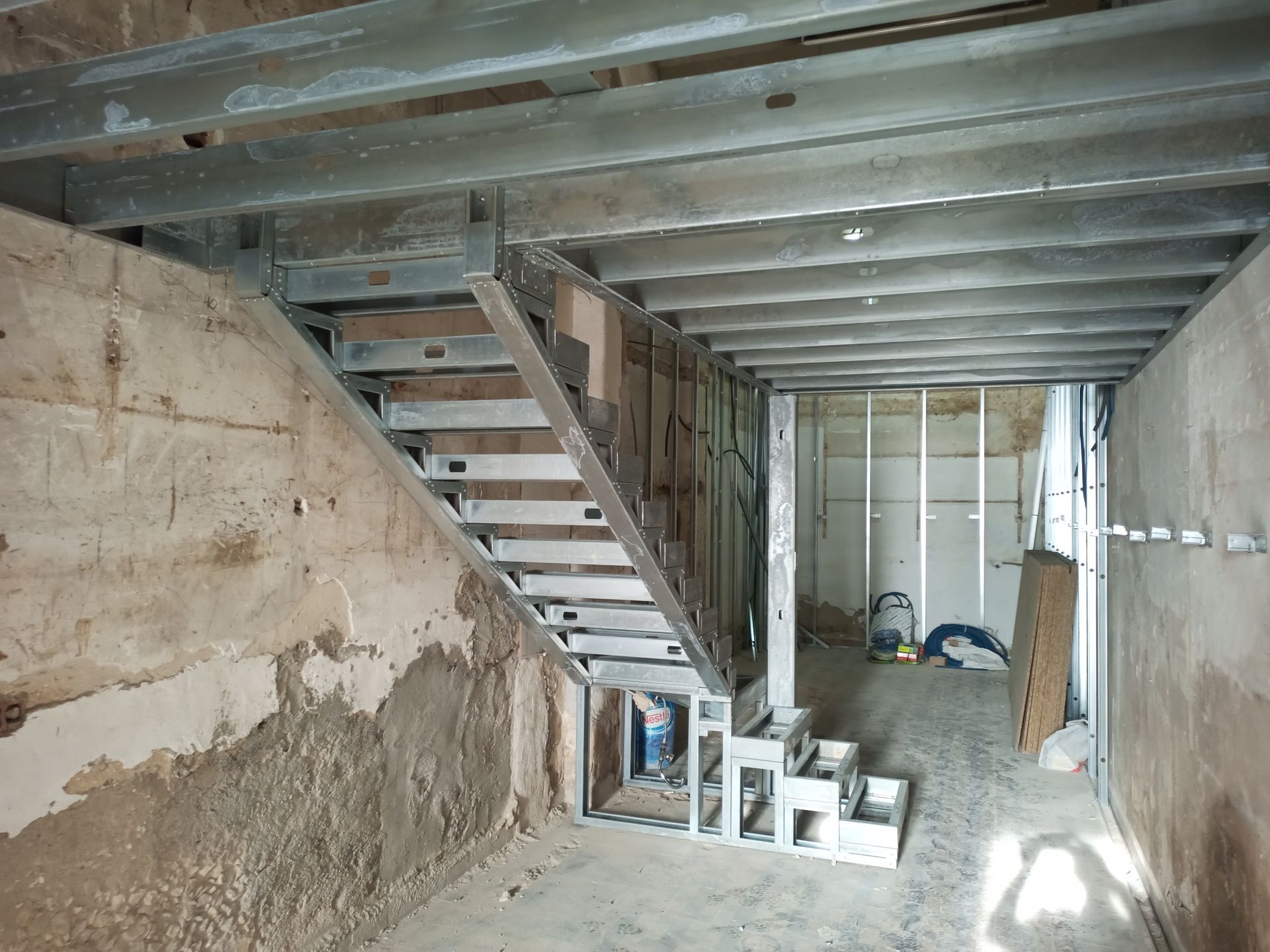 Interior de um canteiro de obras com escada metálica e estrutura aparente.