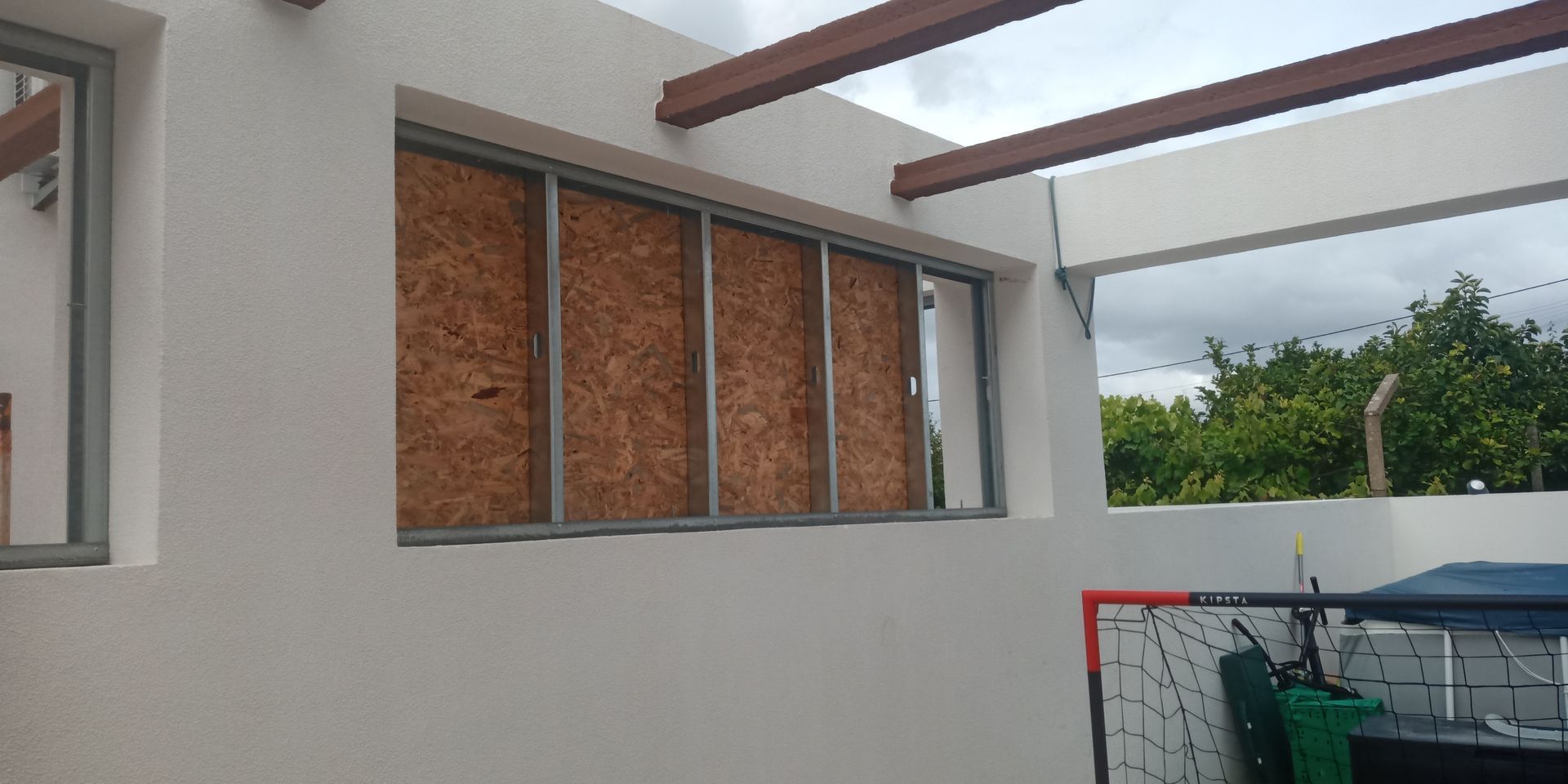 Vista exterior de um edifício com paredes brancas e uma janela coberta por painéis de madeira.