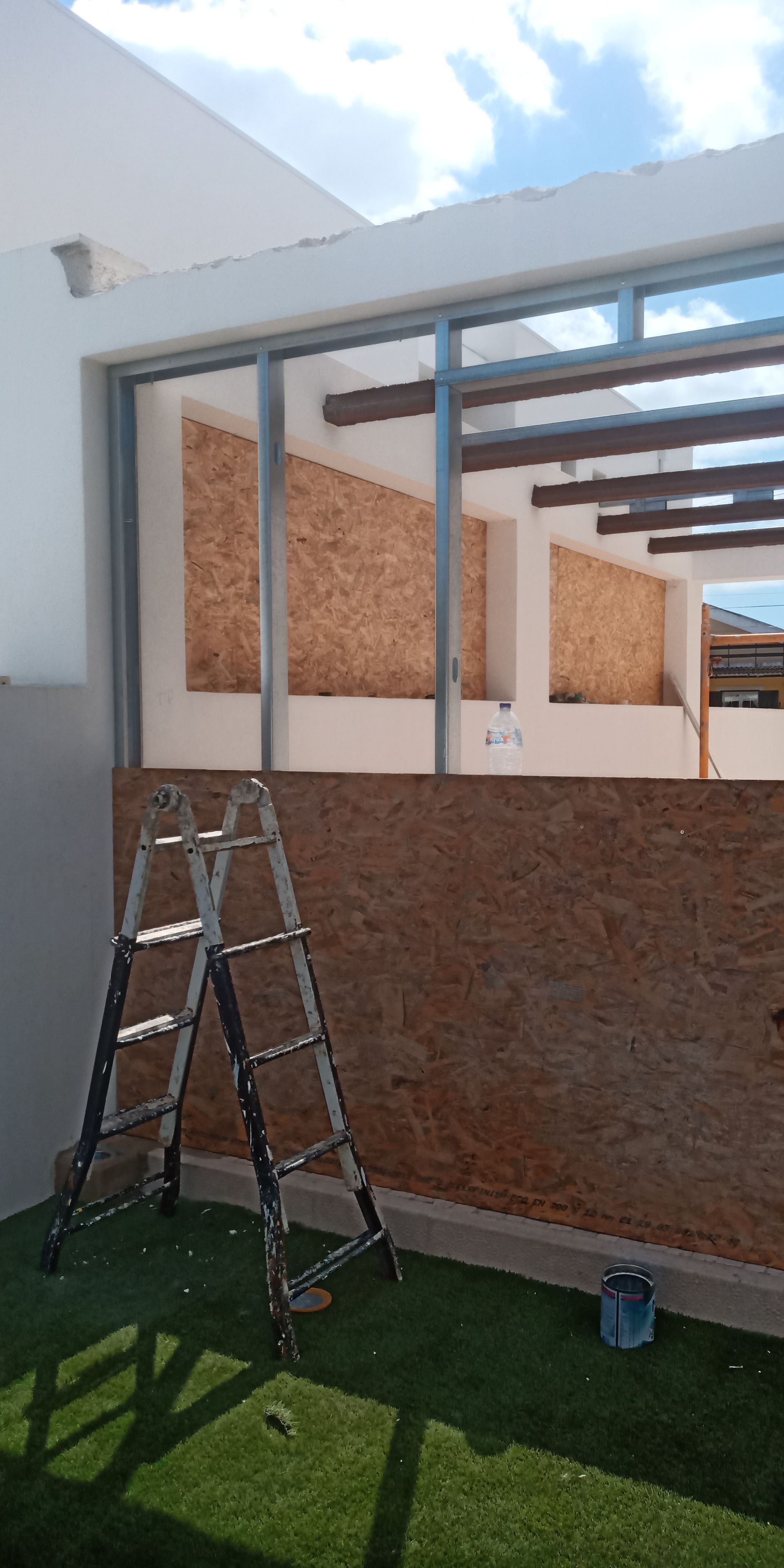 Uma escada metálica está encostada em um prédio em construção, com painéis de madeira expostos e vista para o céu.