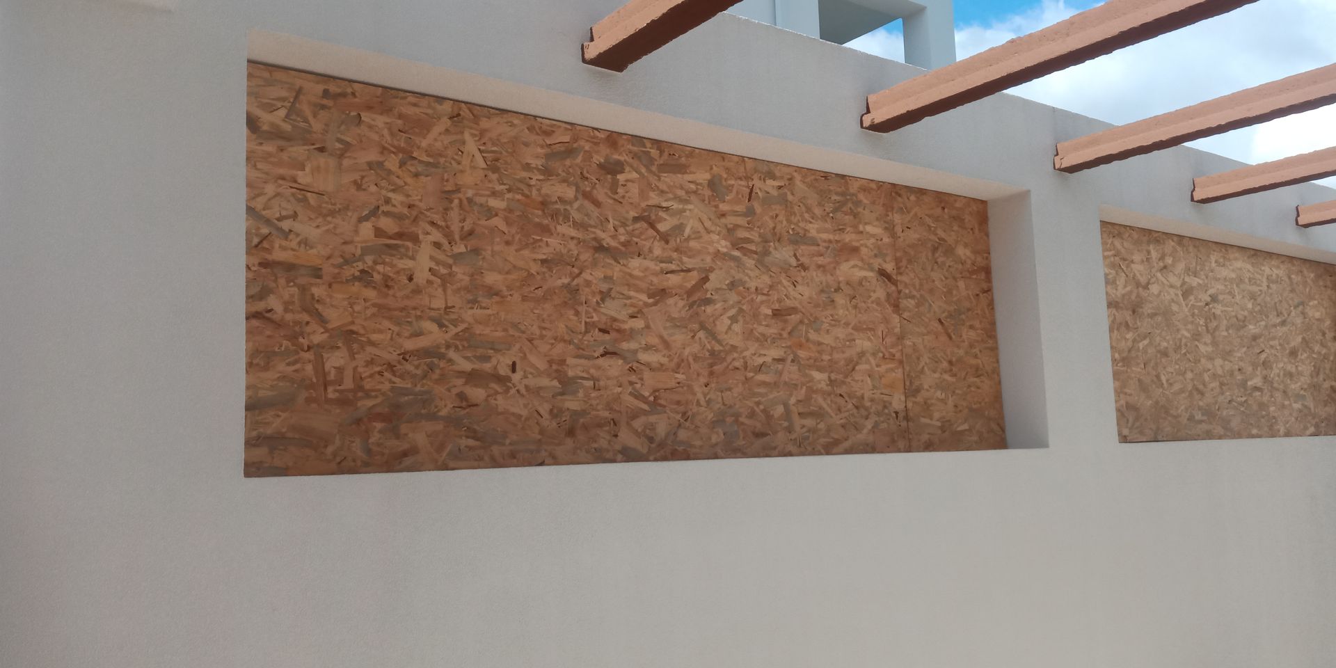 Aberturas retangulares com painéis de madeira marrom, sob um teto e vigas brancas.