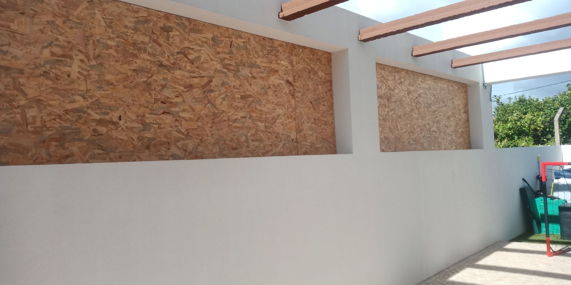 Vista exterior de uma parede com painéis de madeira e uma parede pintada de branco.