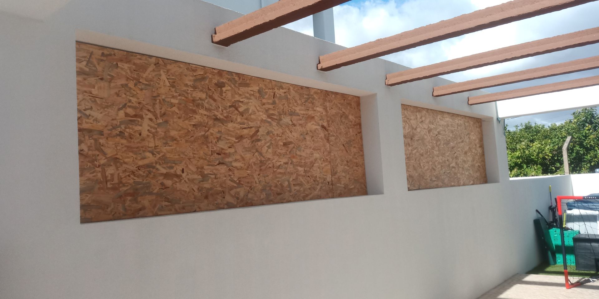 Parede externa com duas seções recuadas revestidas com painéis de madeira. Vigas marrons acima.