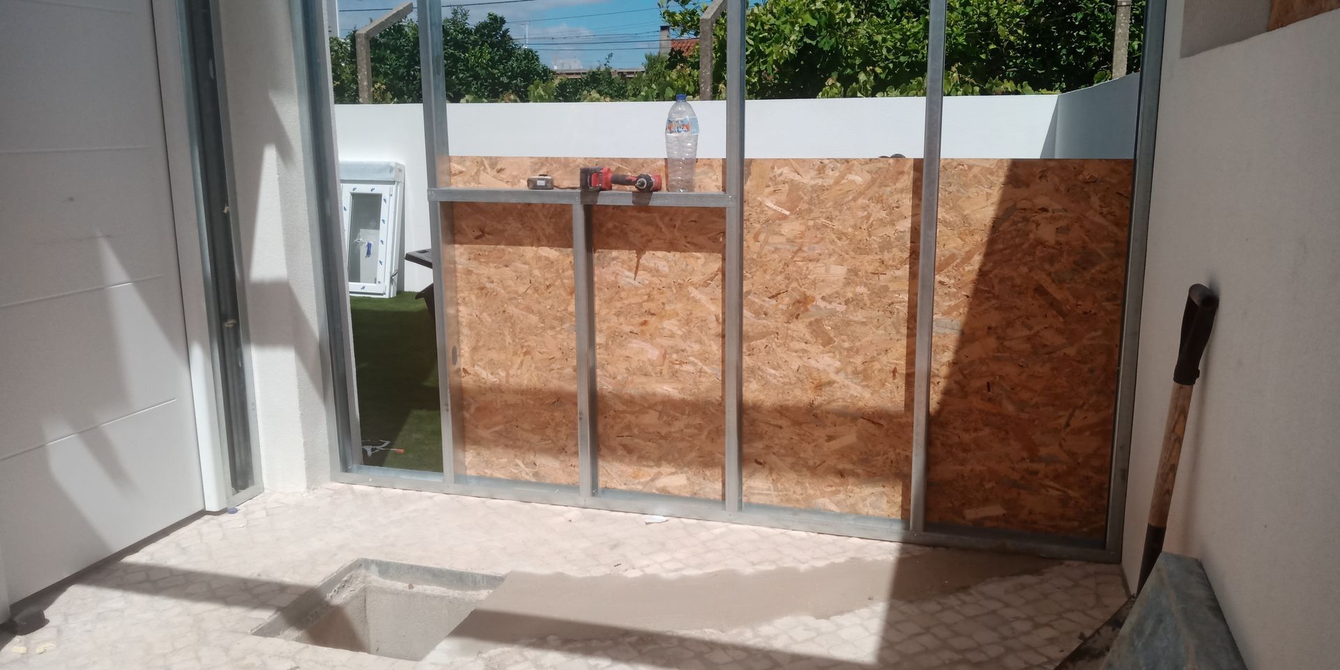 Vista interna de um canteiro de obras com uma parede de madeira em construção com estrutura metálica, cercada por paredes brancas.