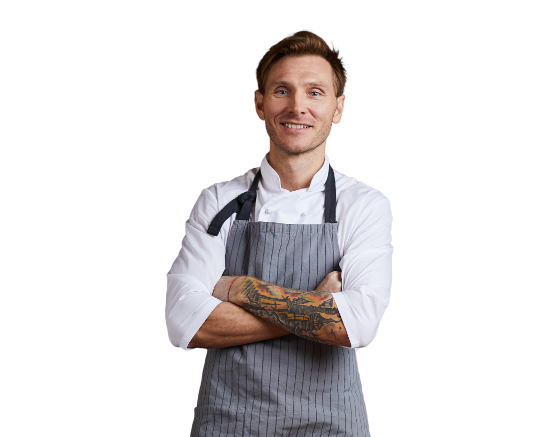 A man in an apron is standing with his arms crossed.