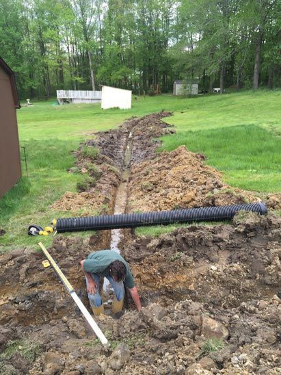 A man is kneeling in the dirt next to a large pipe.