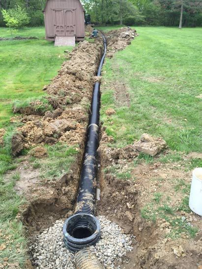 A drain pipe is being installed in the dirt in a yard.