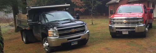 Two dump trucks are parked next to each other in a grassy yard.