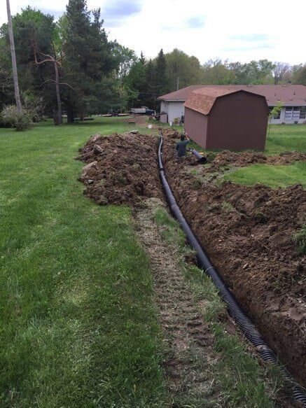 A drain pipe is being installed in a yard next to a barn.