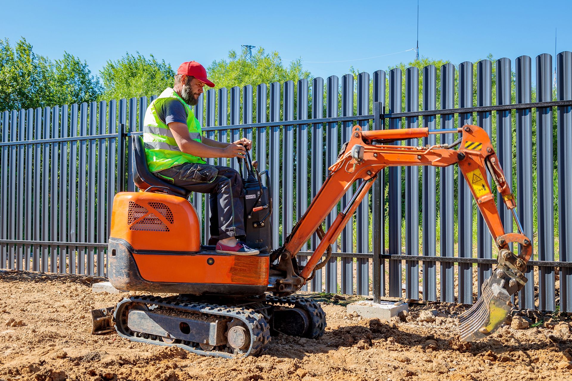A man is driving a small excavator on a dirt field.