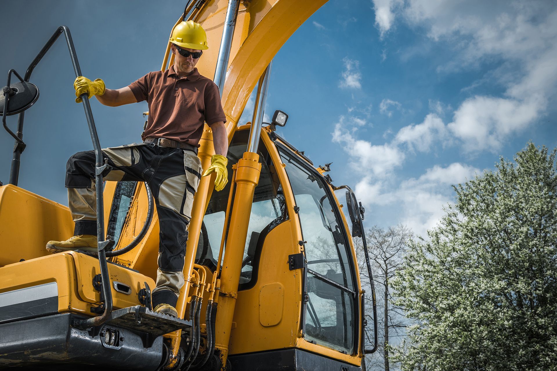 A man is sitting on top of a yellow excavator.