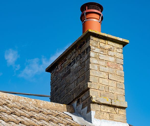a brick chimney on top of a tiled roof with a blue sky in the background .