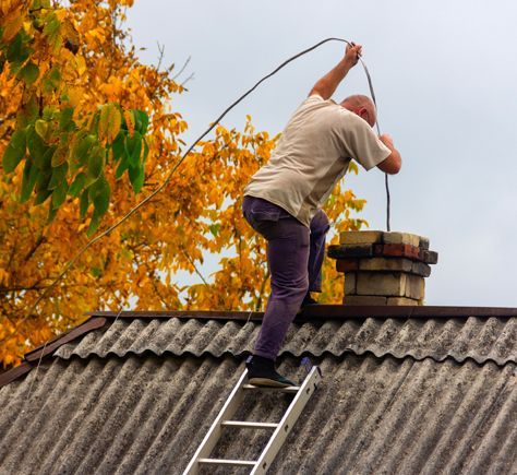 a man is standing on a ladder on top of a roof cleaning a chimney .