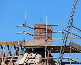 a brick chimney is being built on top of a building with scaffolding .