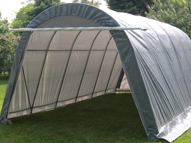 A large gray garage is sitting on top of a lush green field