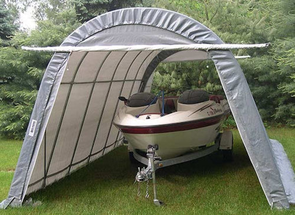 A boat is parked under a garage in the grass.