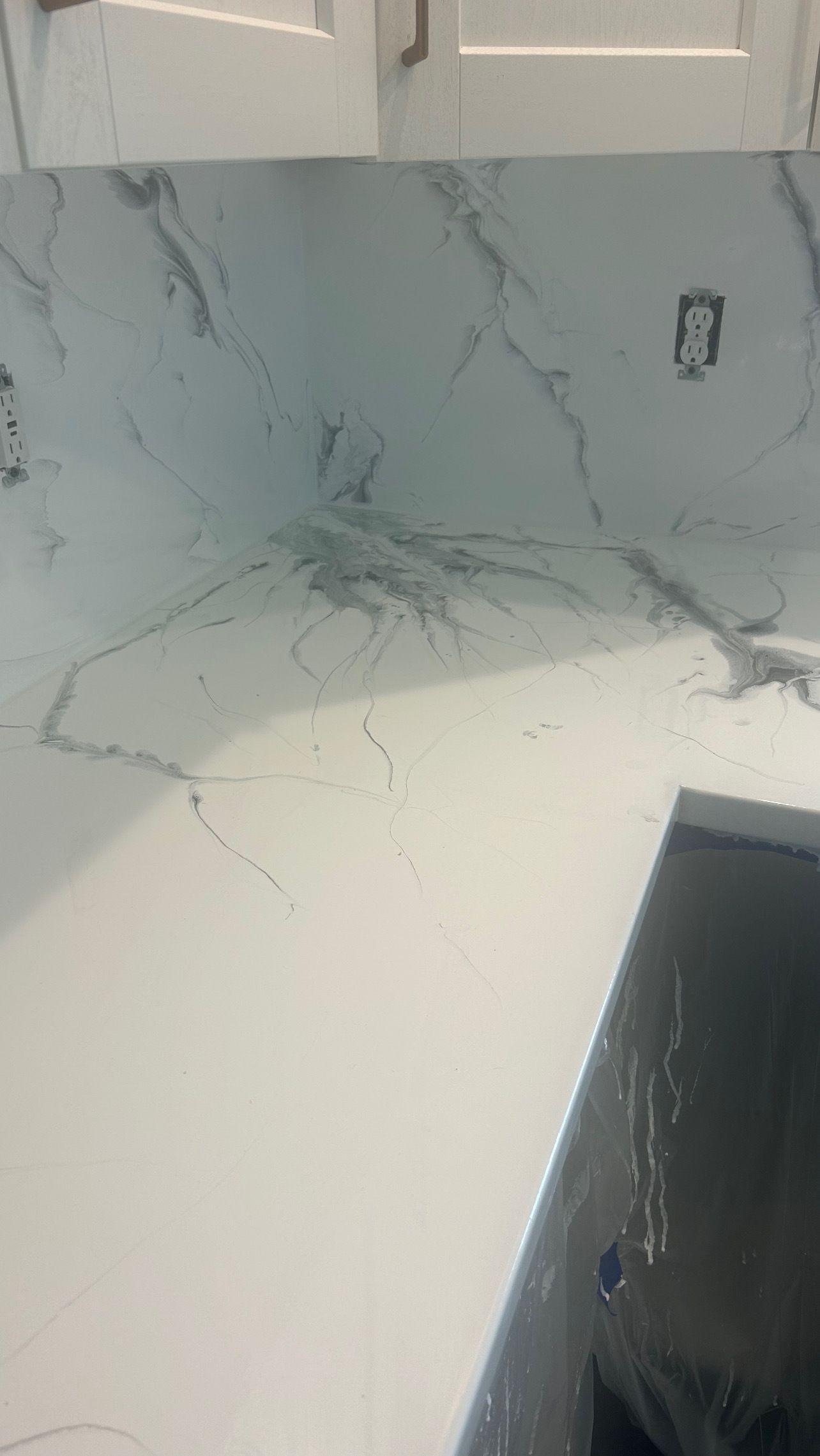 A close-up of a modern grey stone countertop with a textured edge, set above dark matte cabinets in a kitchen.