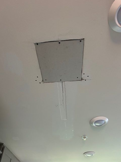 A square patch in a white ceiling with visible screw holes and a long, thin crack extending downward.
