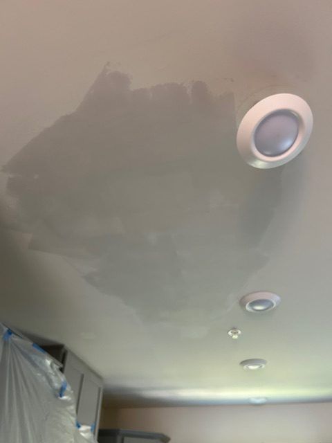 A hand holds a trowel, applying textured gray plaster or cement onto a wall surface.