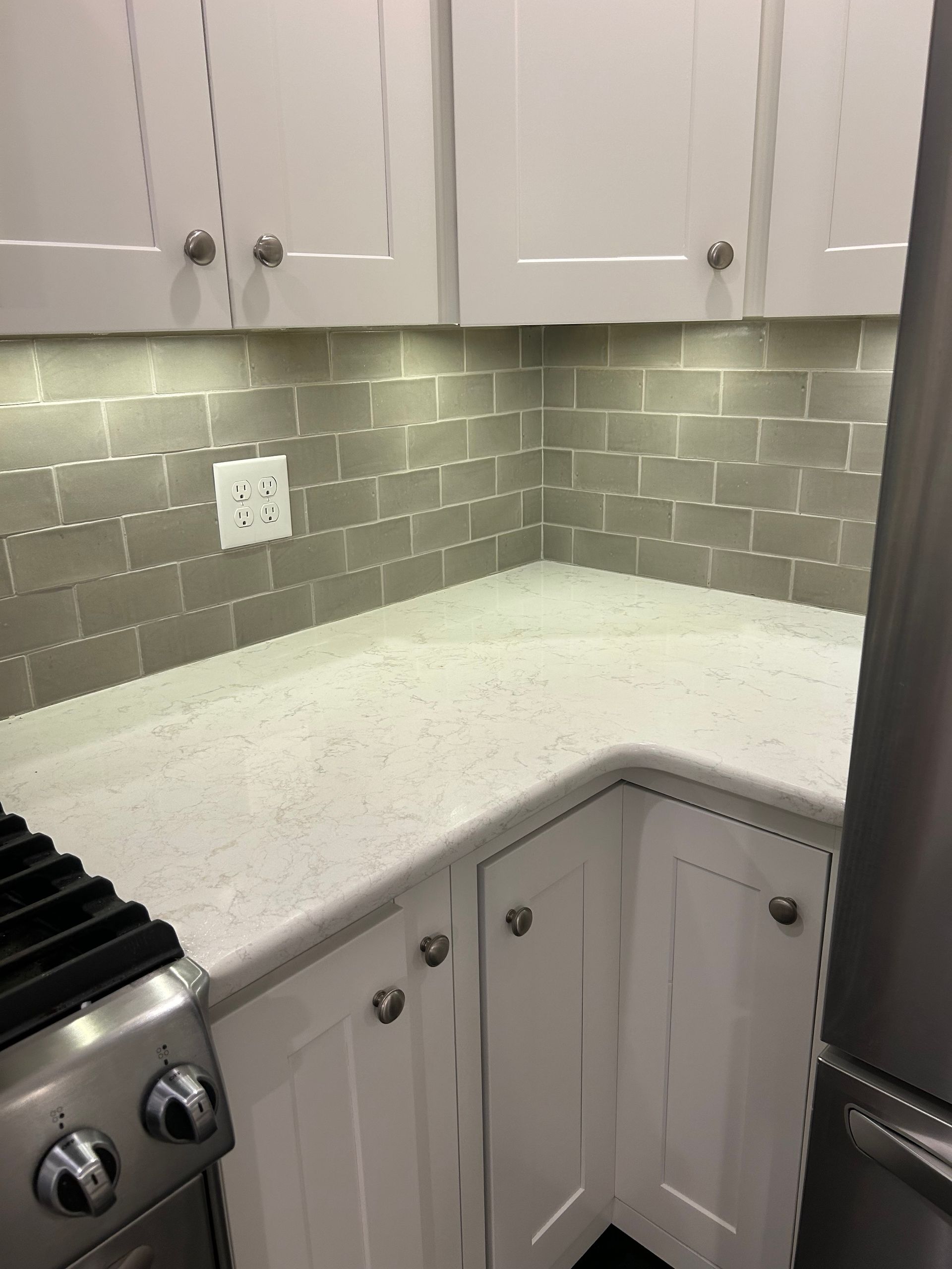 A corner of a kitchen showing white cabinets, a light-speckled countertop, and grey subway tile backsplash.