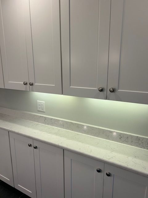 A gloved hand uses a wide plastering trowel to apply a layer of grey compound onto a textured, light-colored wall.