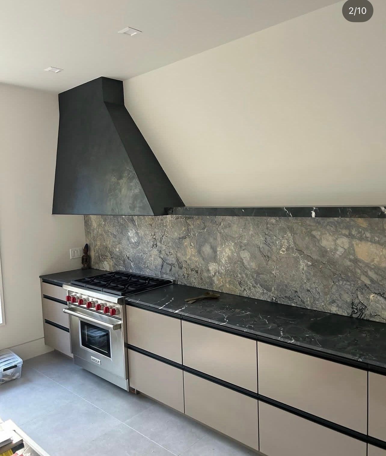 Modern kitchen featuring tan flat-panel cabinets, a black stone countertop and backsplash, and a black range hood.