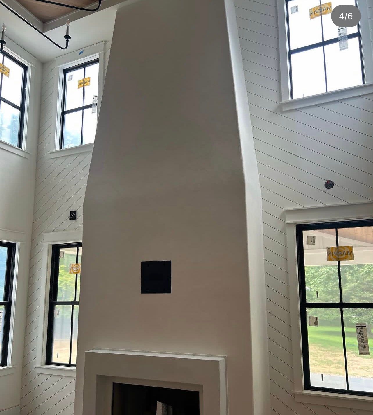 A large, white, tapered fireplace chimney stands between tall, black-framed windows in a room with diagonal-patterned walls.