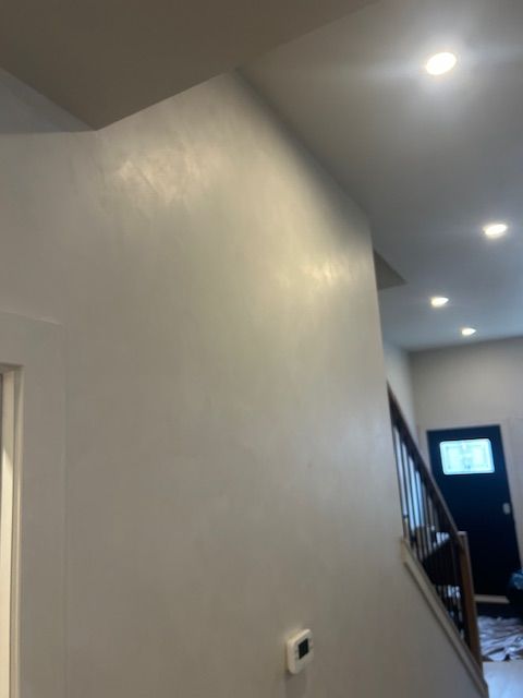 A light gray wall in an entryway featuring a recessed staircase and a dark door in the background.